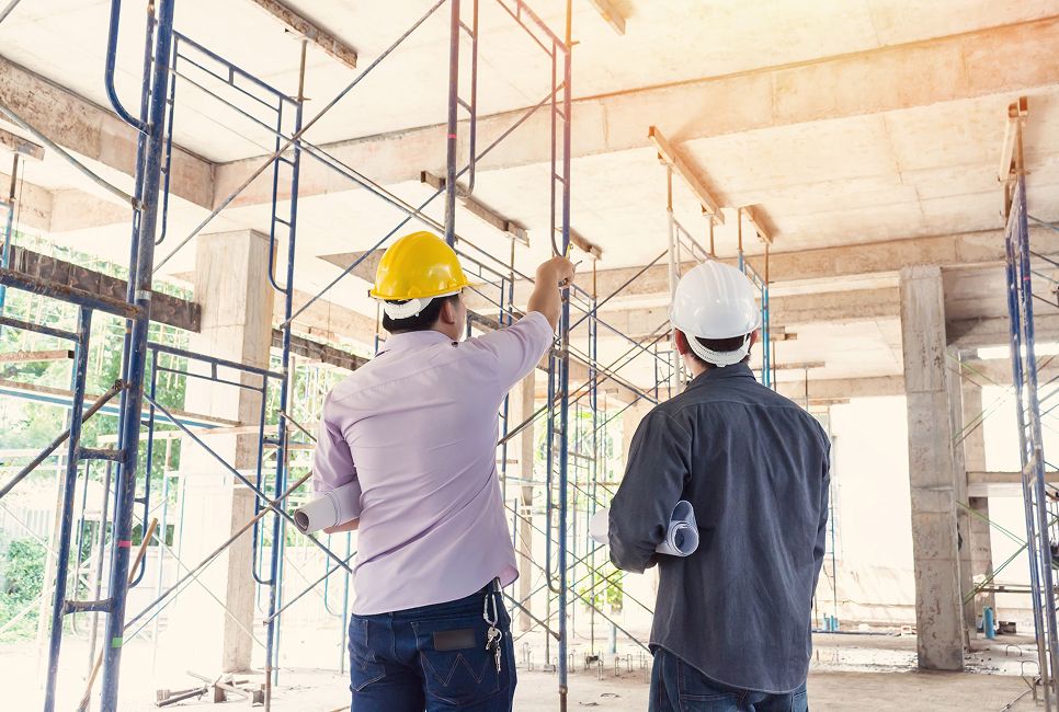 Zwei Bauarbeiter mit Schutzhelmen inspizieren eine Baustelle mit Gerüsten